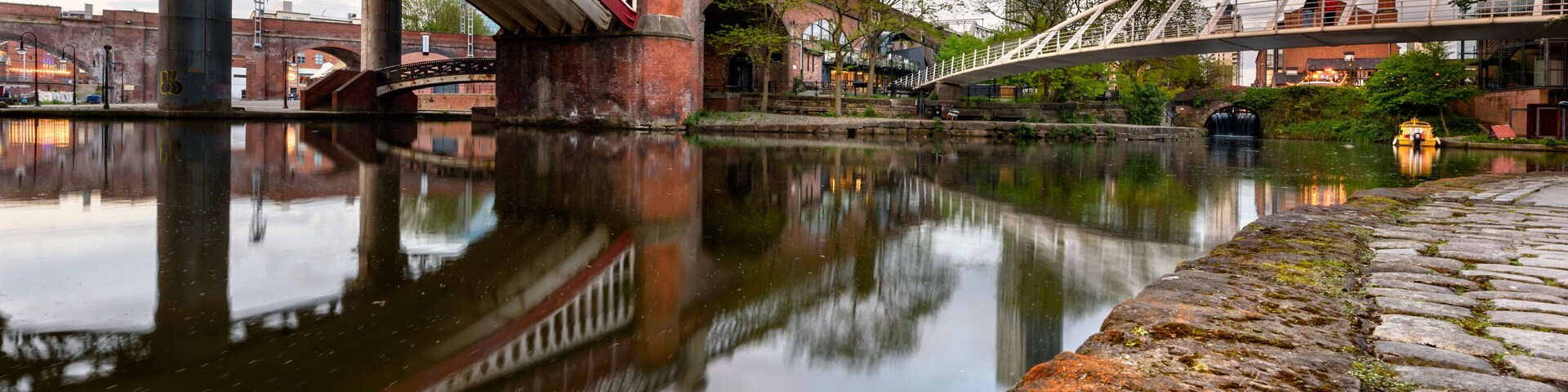 A river with a bridge, stone wall, and a modern building in the background.