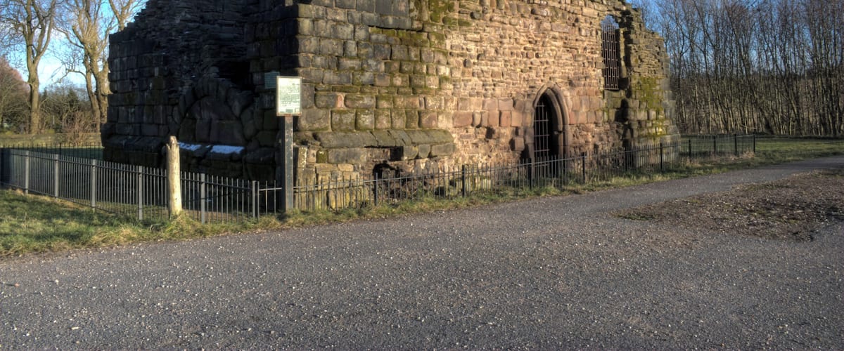 A historic stone building with a collapsed roof and a metal gate.