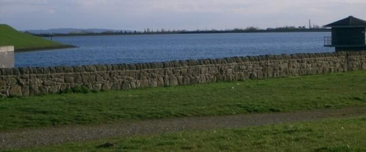 A stone wall, grassy field, and a body of water with a distant shoreline.