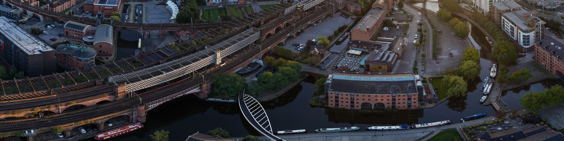 Panoramic sunrise aerial view of Castlefield in Manchester featuring the Bridgewater Canal, viaducts, and Merchants’ Warehouse.