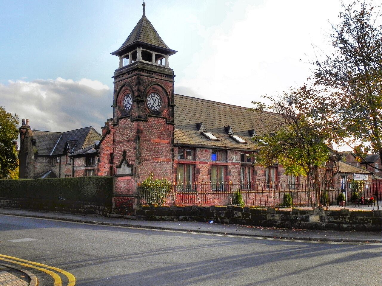 A historic building with a clock tower, brick walls, and a small garden.