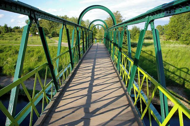 A green metal bridge with yellow railings over a river.