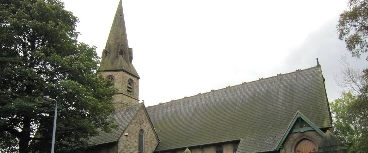 A church with a tall steeple and a green fence in front.