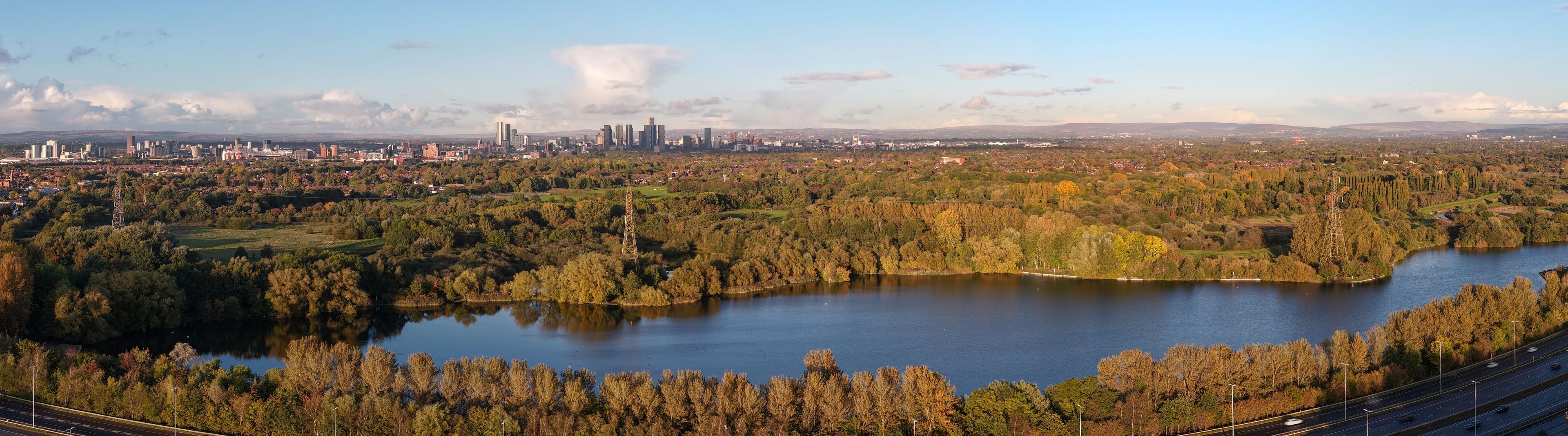 A lake surrounded by trees and a city skyline in the background.
