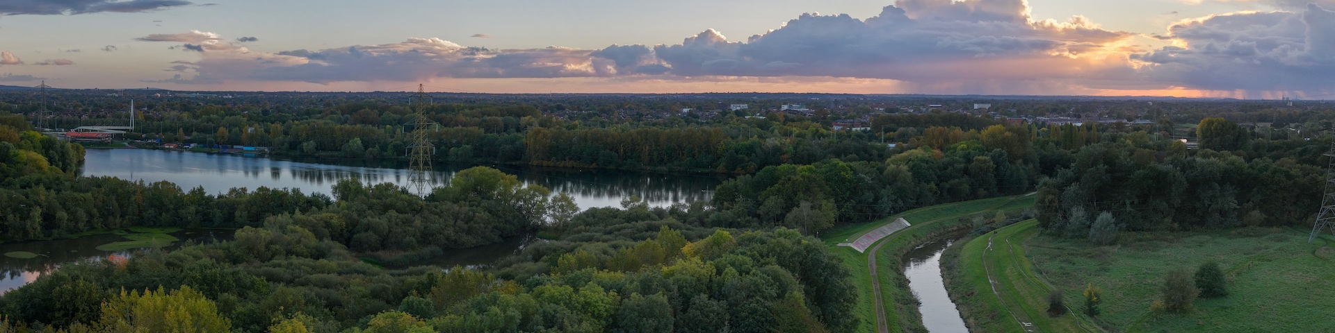 Un río serpentea a través de una zona boscosa densa, con un puente y líneas eléctricas a lo lejos.