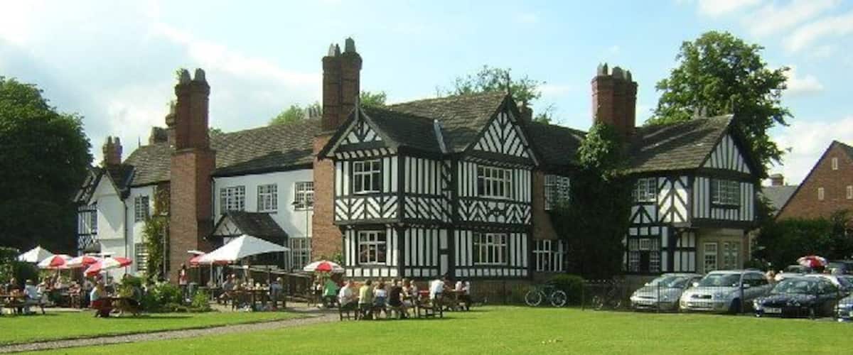 A Tudor-style building with a lawn in front, surrounded by parked cars and people.