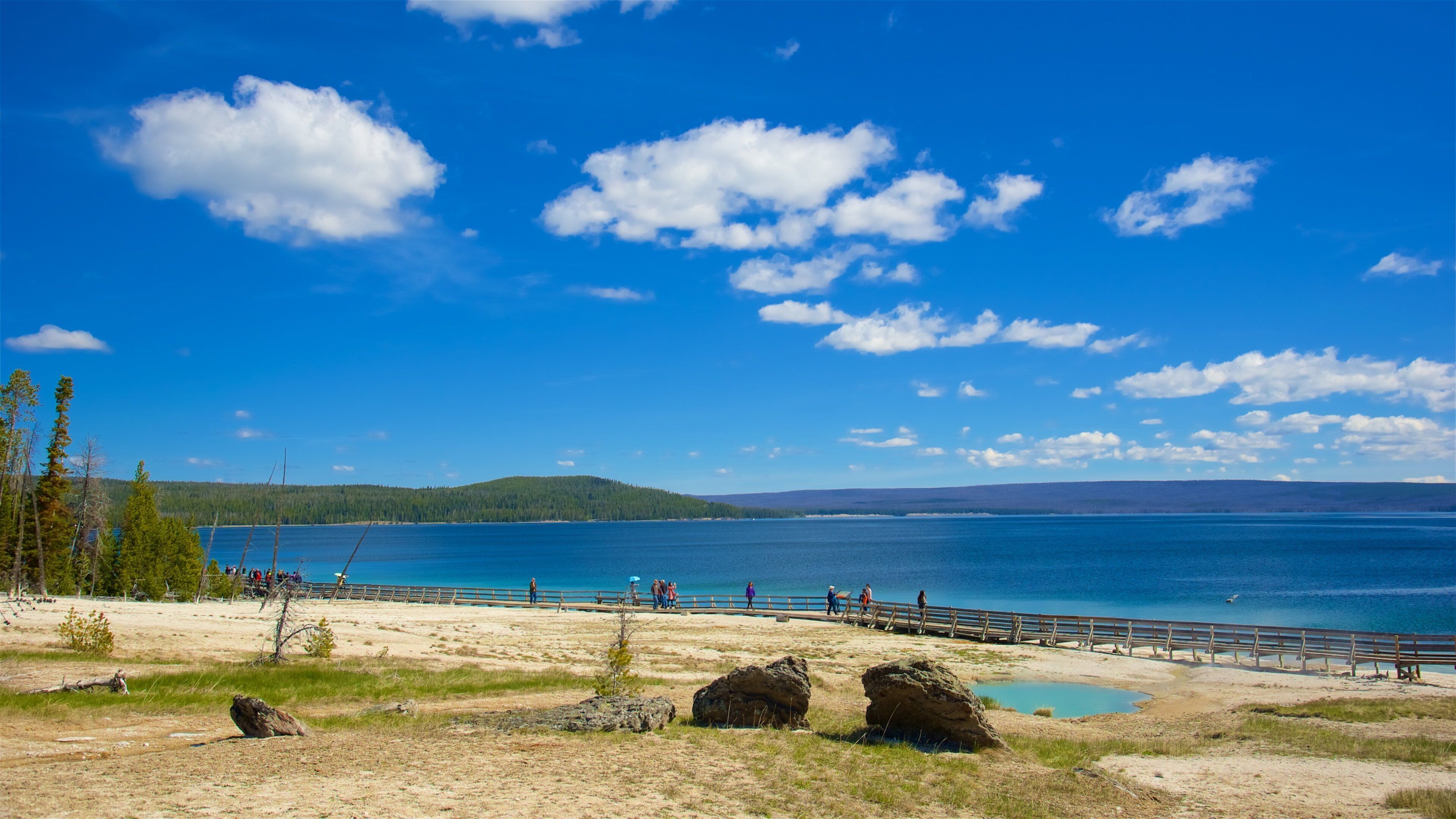 A clear blue lake with a wooden pier, surrounded by trees and rocks.