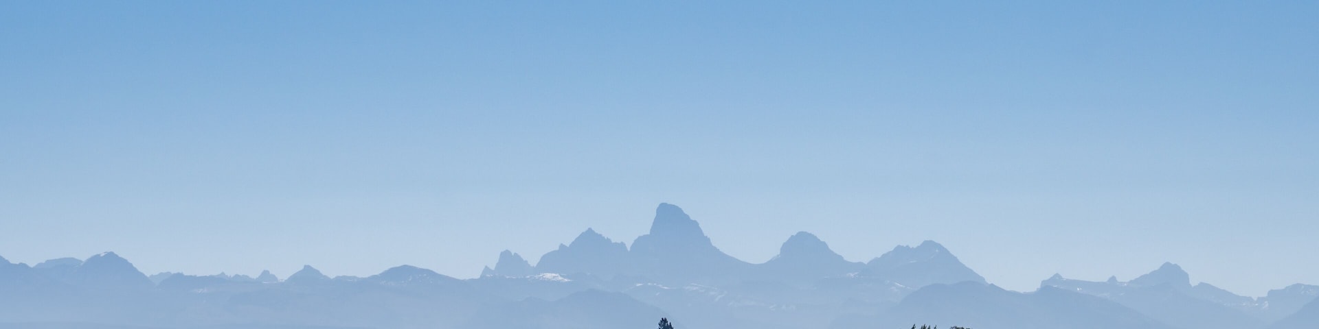 A rural landscape with fields, a small house, and distant mountains under a clear sky.