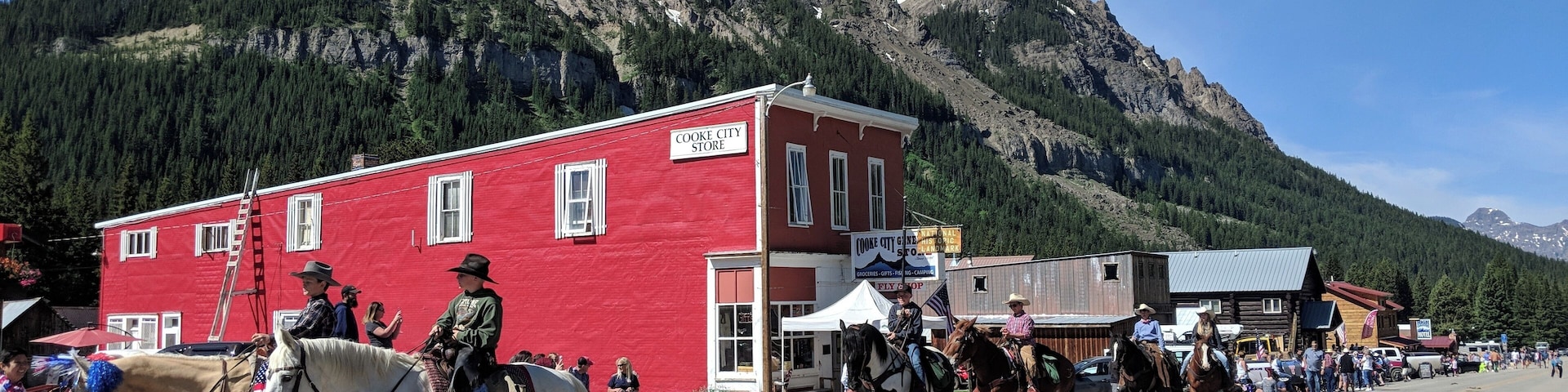 A street parade with people on horseback, a red building labeled 'COOKE CITY STORE', and a mountainous backdrop.