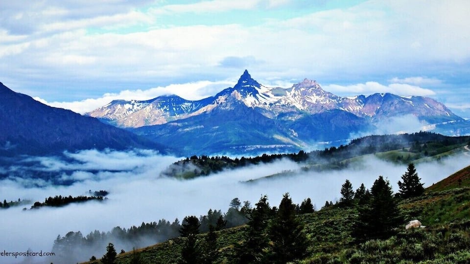 A mountain range with a prominent peak, forested valley, and mist-covered terrain.