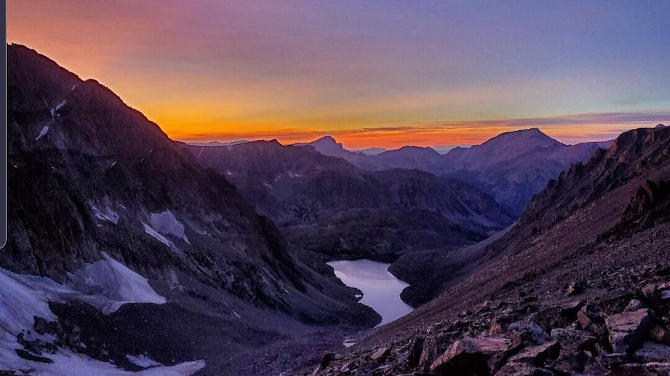 A mountain landscape with a valley and a lake at sunset.