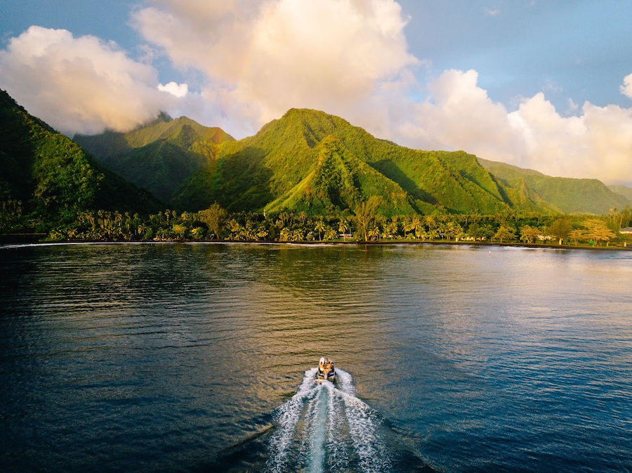 A boat on a calm sea with lush green mountains in the background.