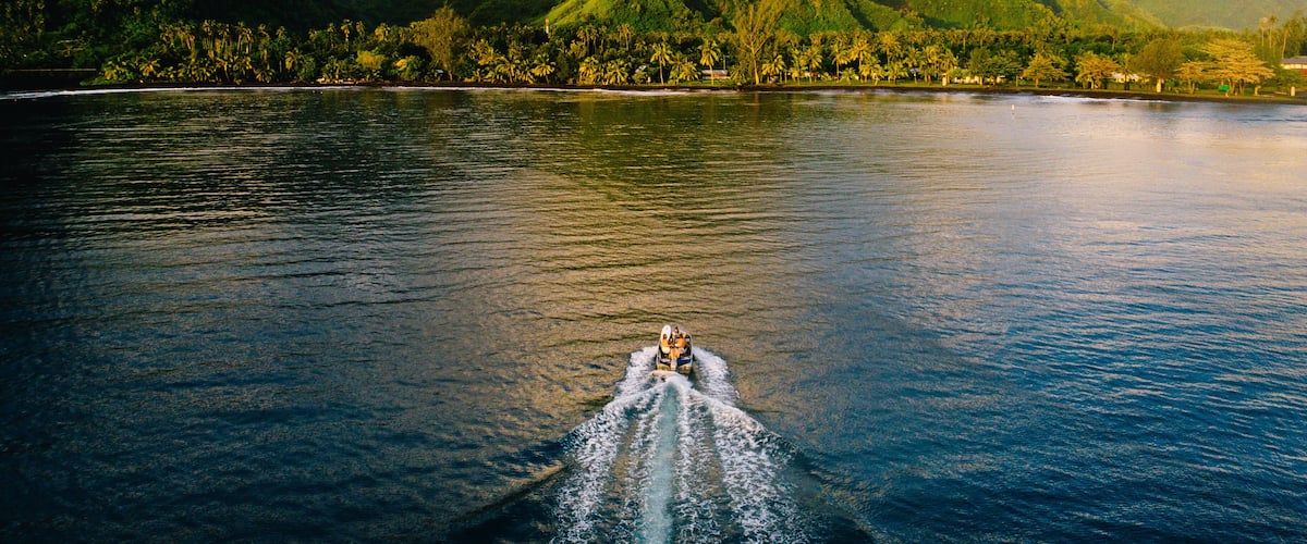 A boat on a calm sea with lush green mountains in the background.