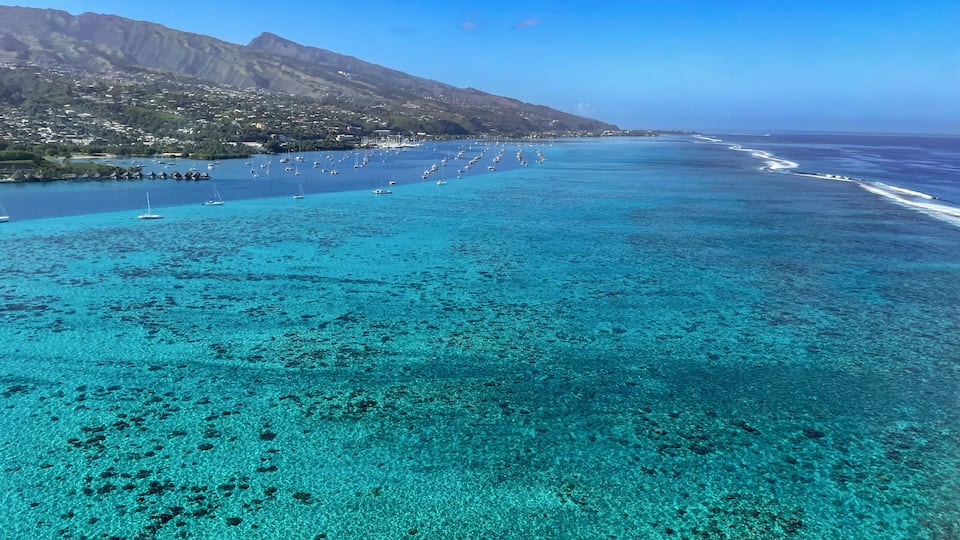 A coastal landscape with clear turquoise waters, a marina with boats, and a mountainous backdrop.