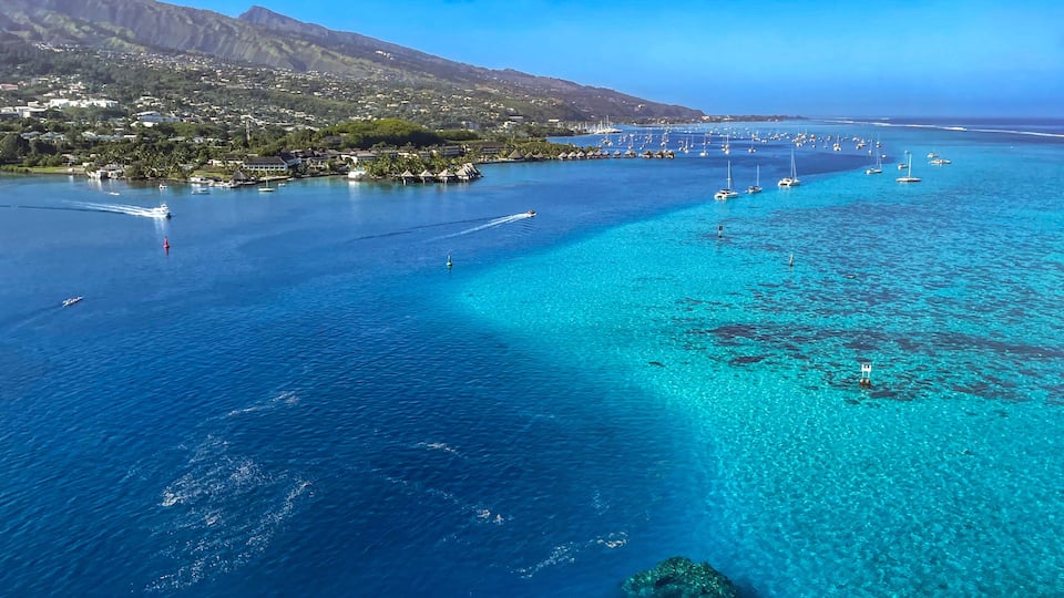 A coastal town with clear turquoise waters, boats, and a mountainous backdrop.