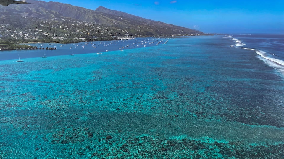 A coastal landscape with clear turquoise waters, a mountainous backdrop, and a marina with boats.