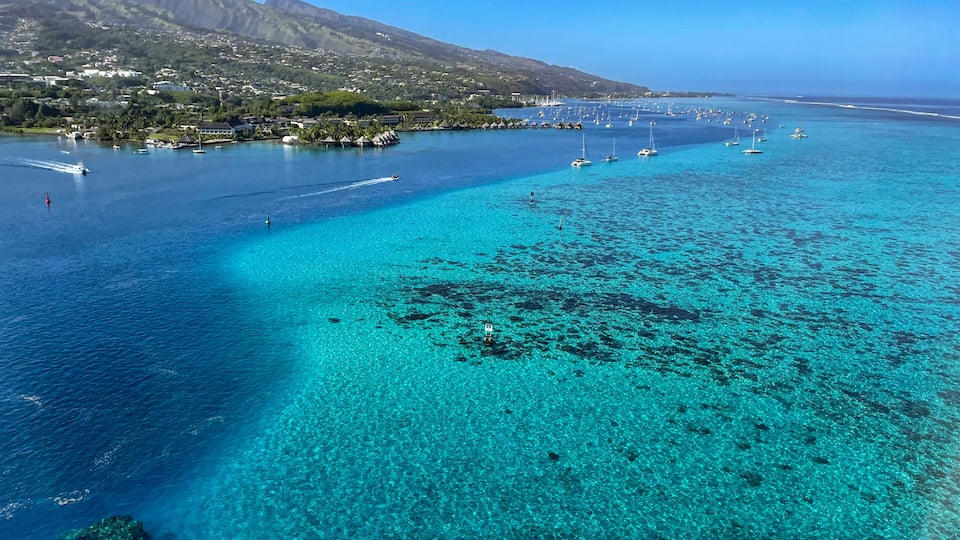 A coastal town with clear turquoise waters, boats, and a mountain in the background.