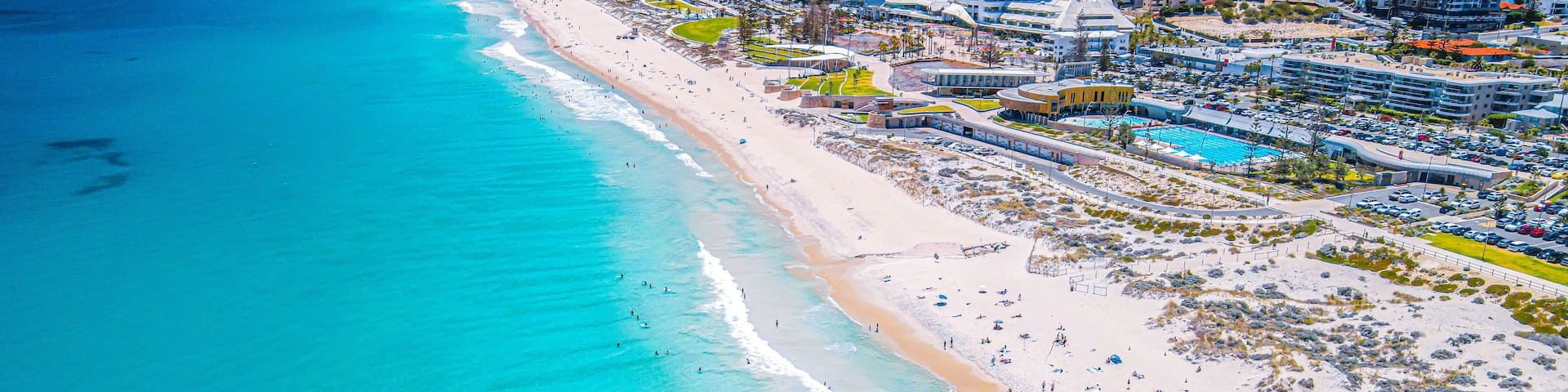 A coastal cityscape with a long sandy beach, clear turquoise waters, and a dense cluster of hotels and buildings.