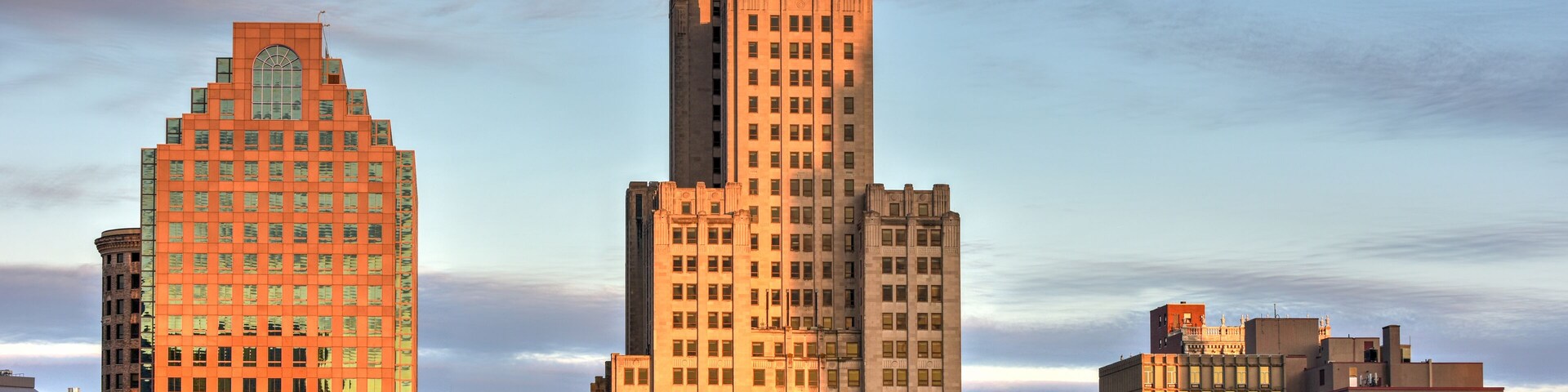 Paisagem urbana com edifícios altos, incluindo um imponente arranha-céu em estilo Art Déco e um arranha-céu moderno.