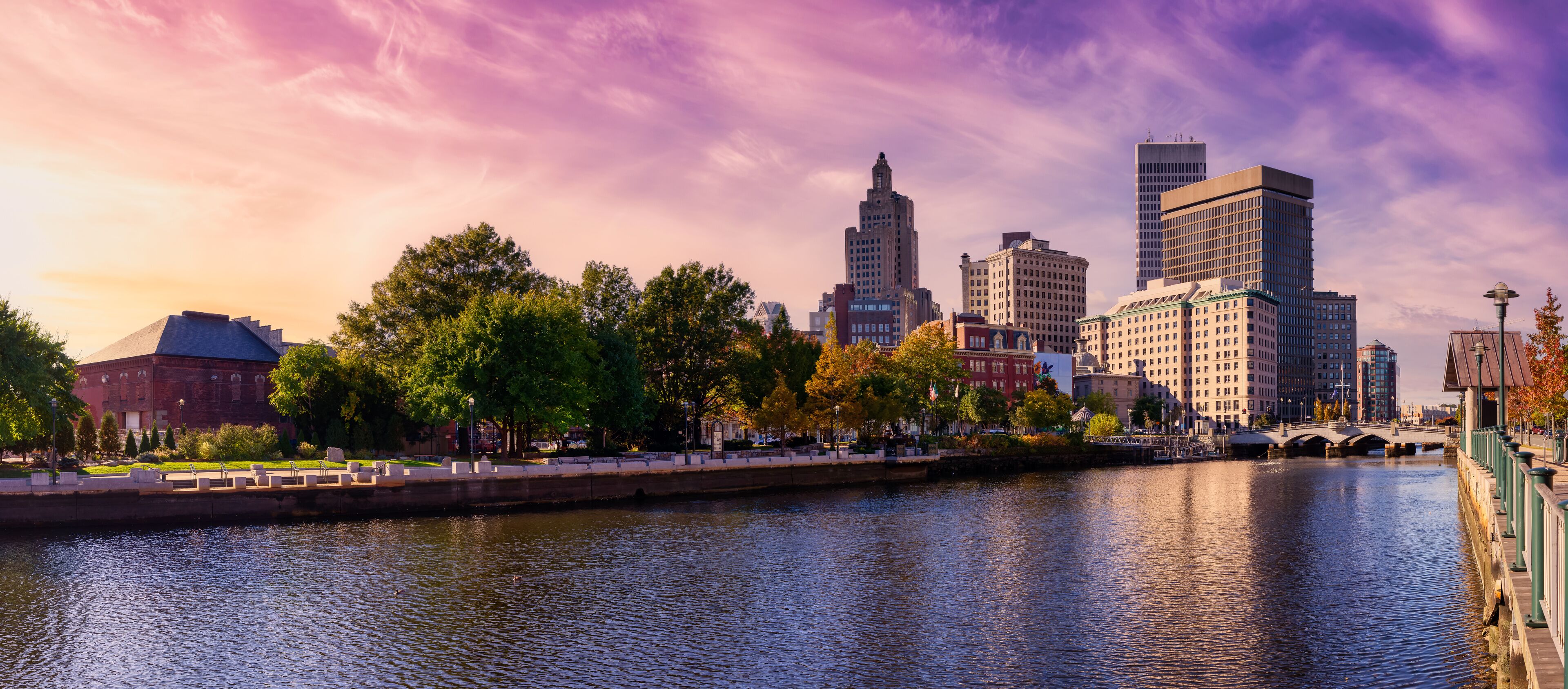 A river with a bridge, a city skyline, and trees.