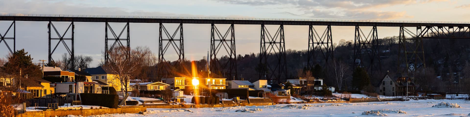A snow-covered landscape with a bridge, houses, and a sunset.