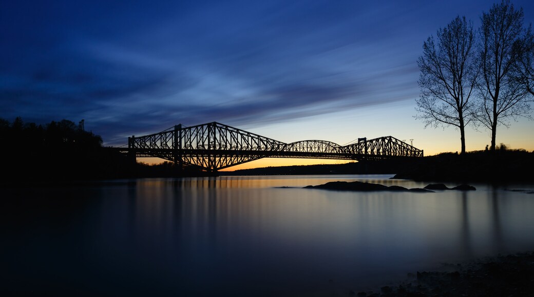Een stalen brug over een rustige rivier in de schemering.