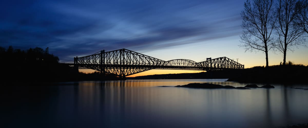 Un pont d’acier enjambant une rivière paisible, au crépuscule.