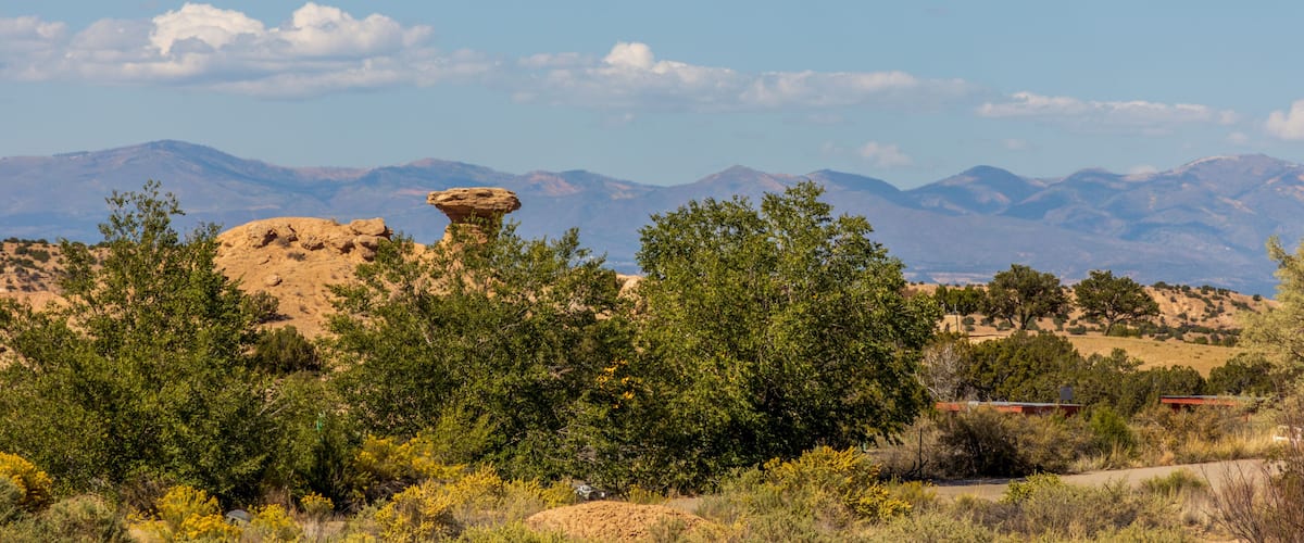 Un paysage désertique avec une formation rocheuse imposante au premier plan, un ciel bleu dégagé et des montagnes à l’horizon.