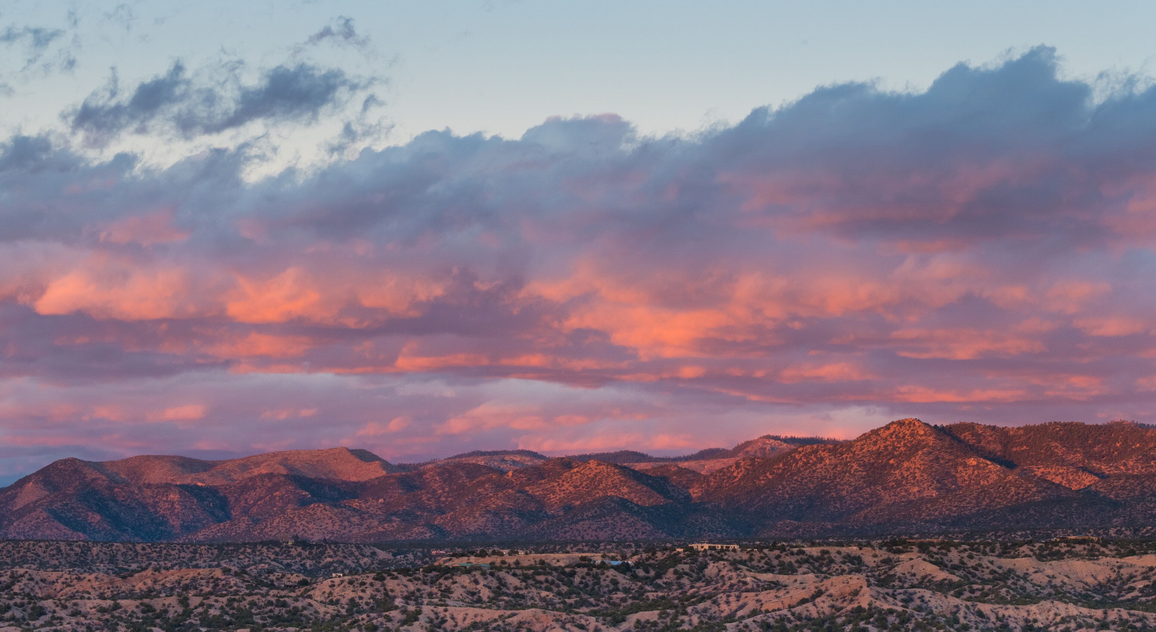 Dramatic, beautiful sunset casts purple and orange colors and hues on clouds and mountains over a neighborhood in Tesuque, near Santa Fe, New Mexico