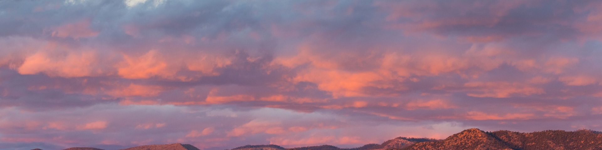 Dramatic, beautiful sunset casts purple and orange colors and hues on clouds and mountains over a neighborhood in Tesuque, near Santa Fe, New Mexico