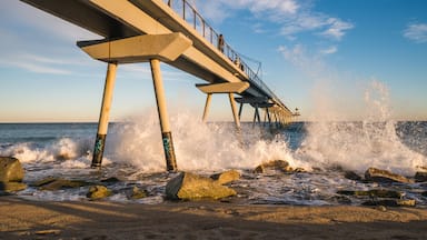 A pier extending into the sea with waves crashing against it, and a clear sky above.