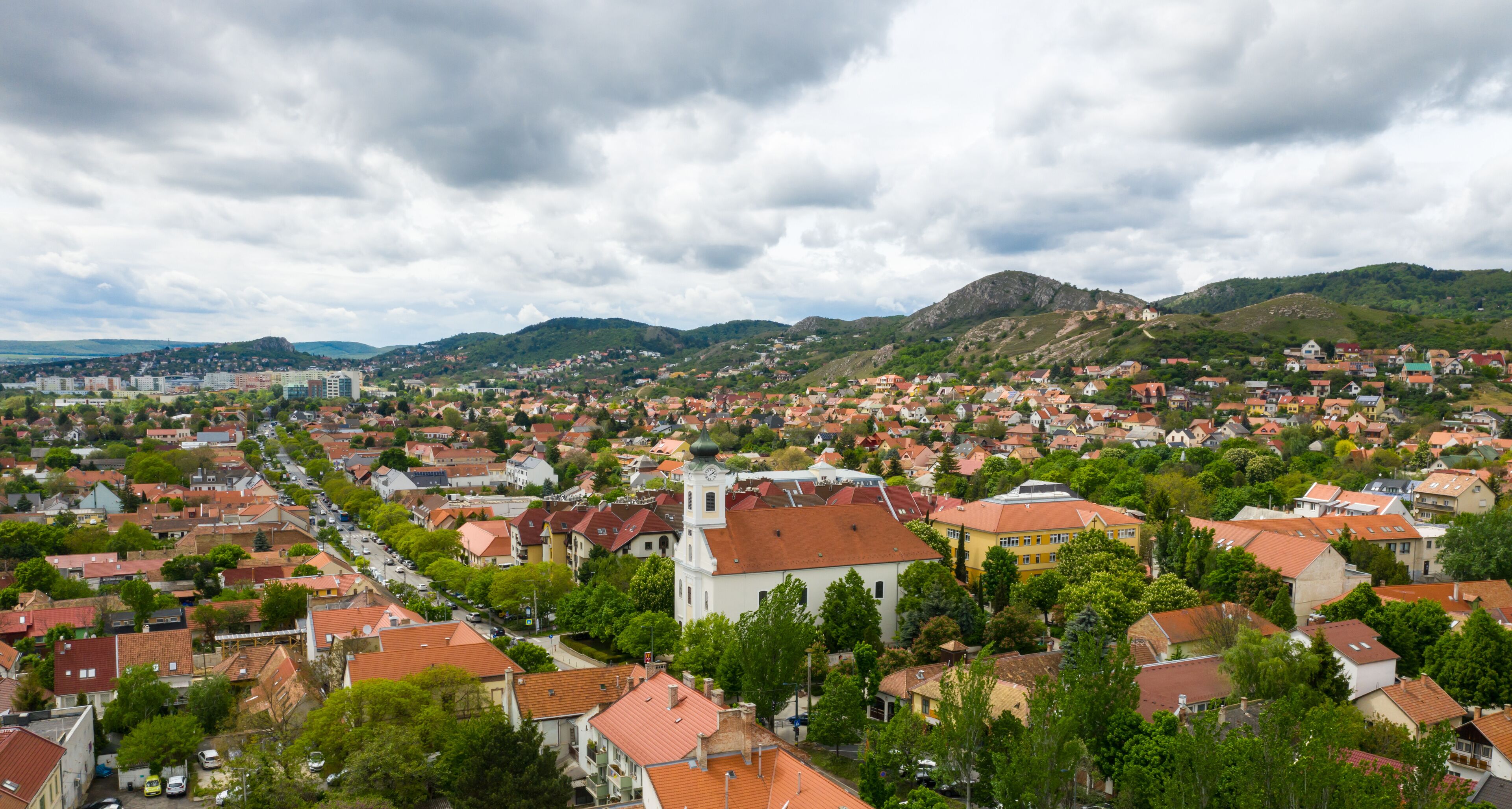 A town with red-roofed houses, a prominent church, and green hills in the background.