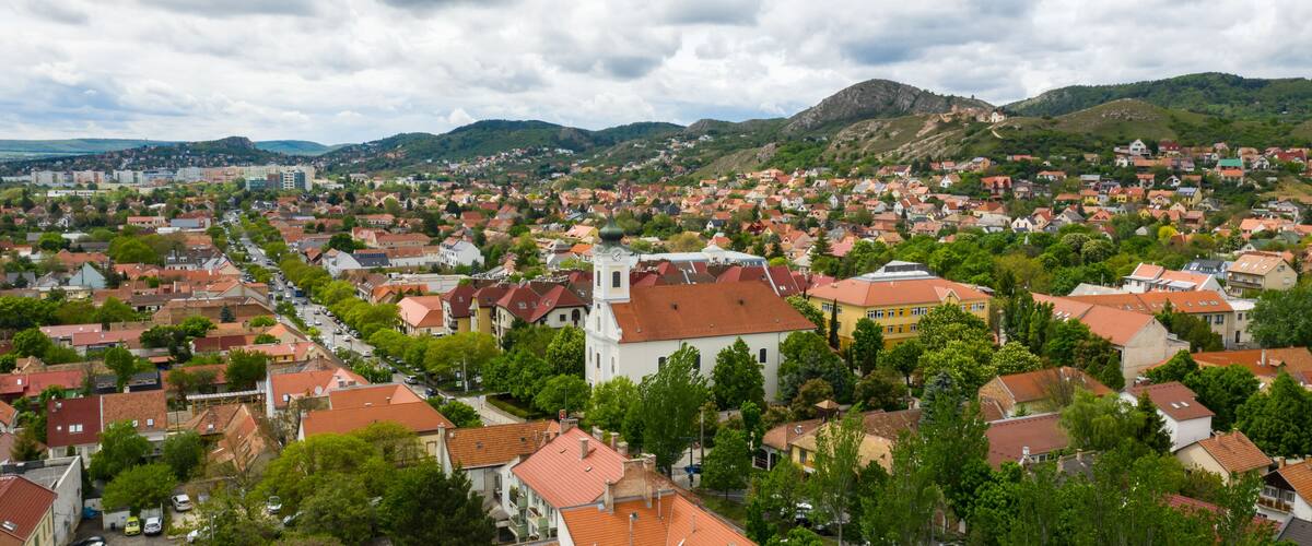 A town with red-roofed houses, a prominent church, and green hills in the background.