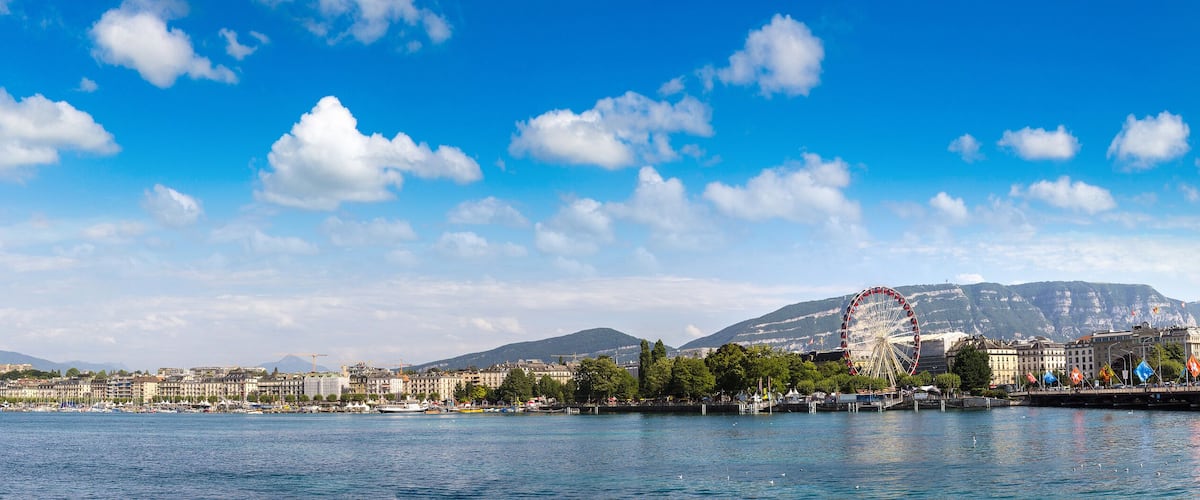 A cityscape with a prominent fountain, a Ferris wheel, and mountains in the background.