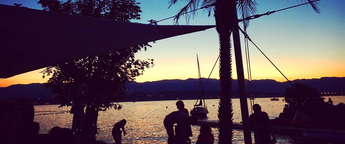 A sunset over a body of water with palm trees and boats.