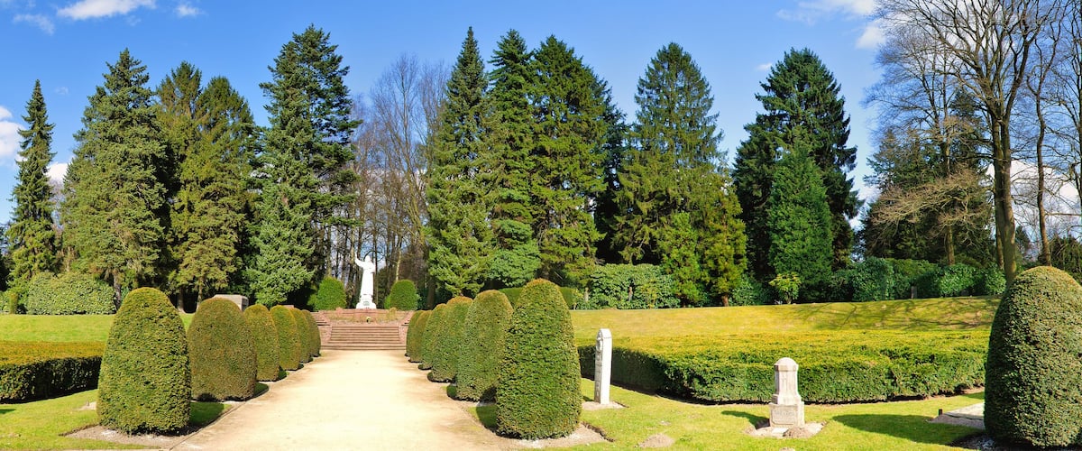Un jardin à la française, avec des haies soigneusement taillées, un chemin central et une statue.