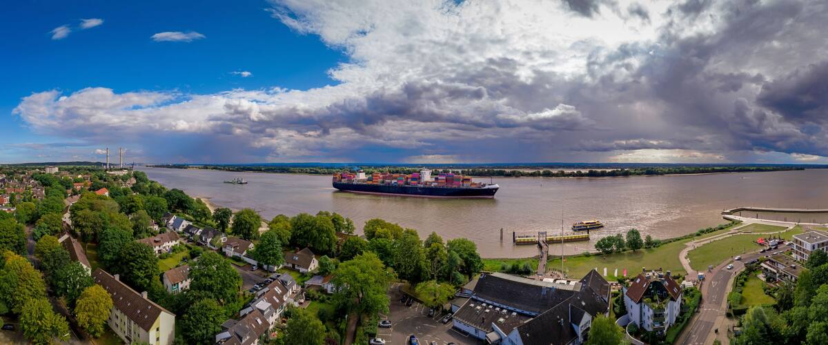 A river with a large cargo ship, a bridge, and surrounding residential areas.