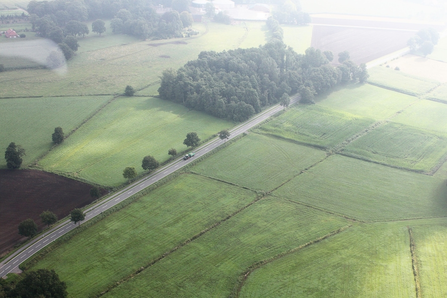 An aerial view of a rural landscape with a road, fields, and a forest.