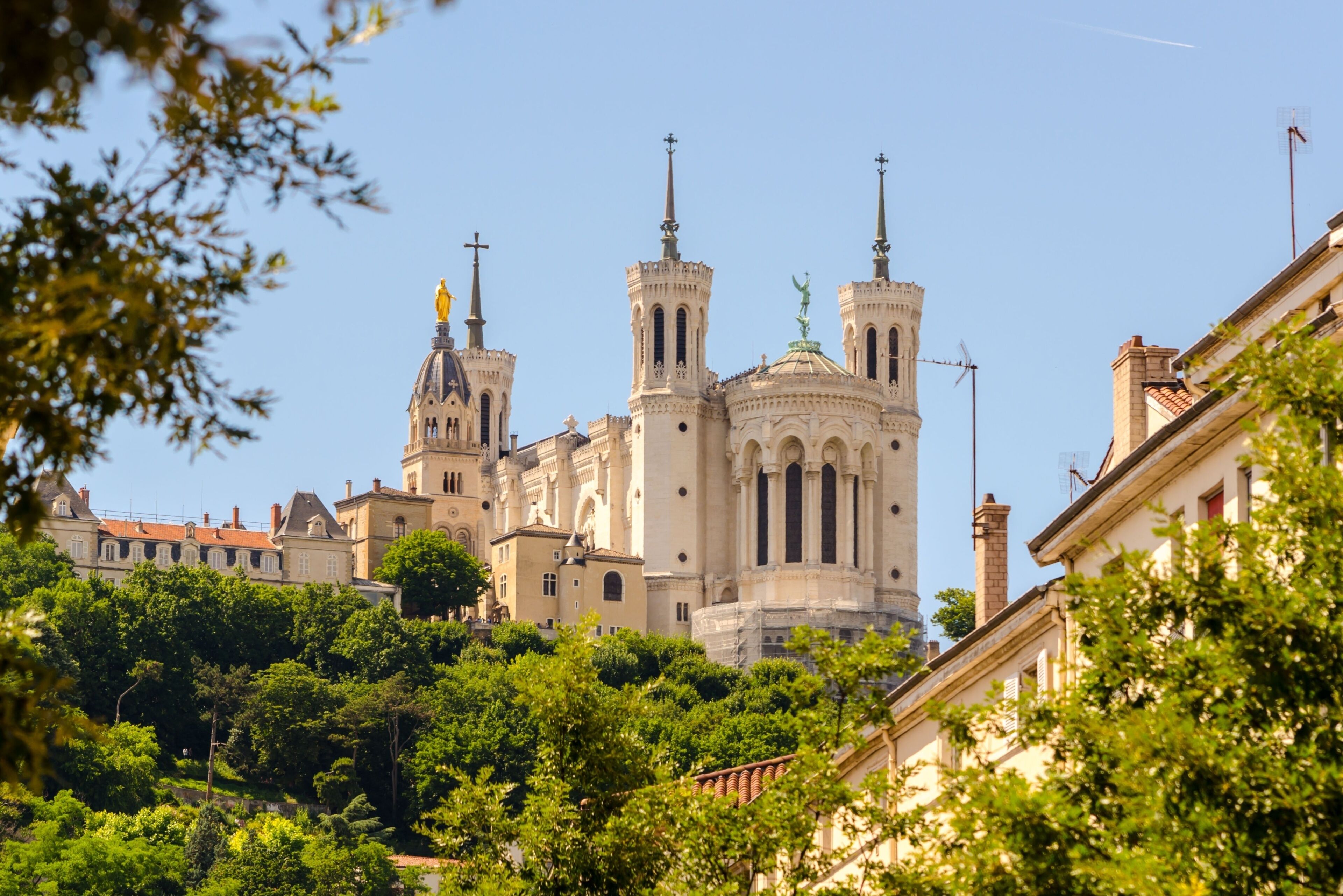 A historic cathedral with twin towers and a dome, surrounded by lush greenery and adjacent buildings.