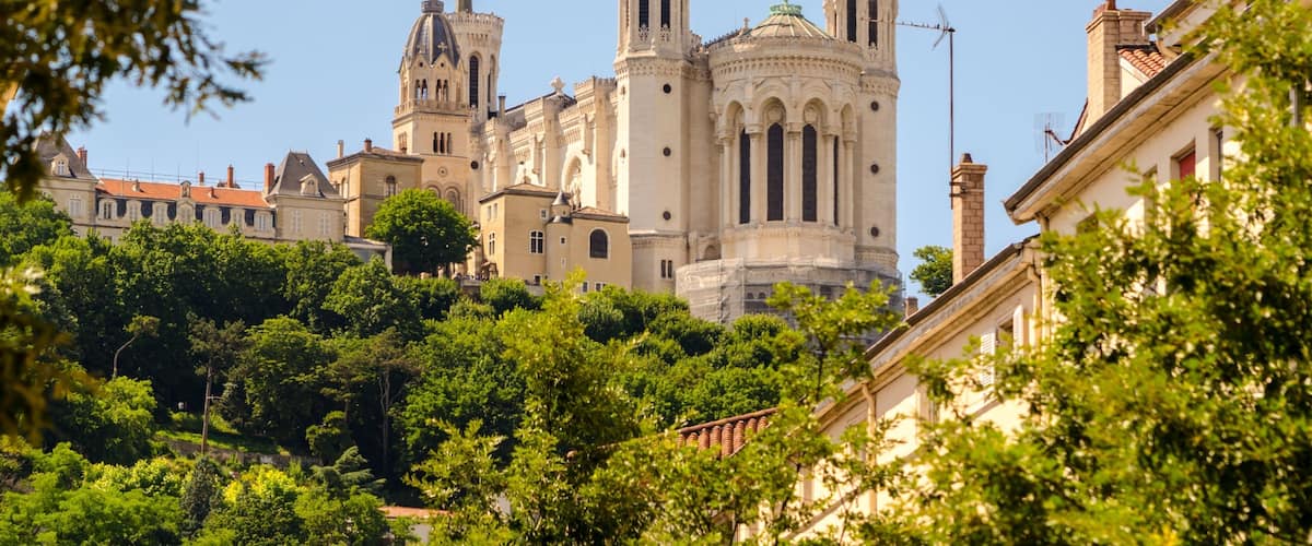 A historic cathedral with twin towers and a dome, surrounded by lush greenery and adjacent buildings.