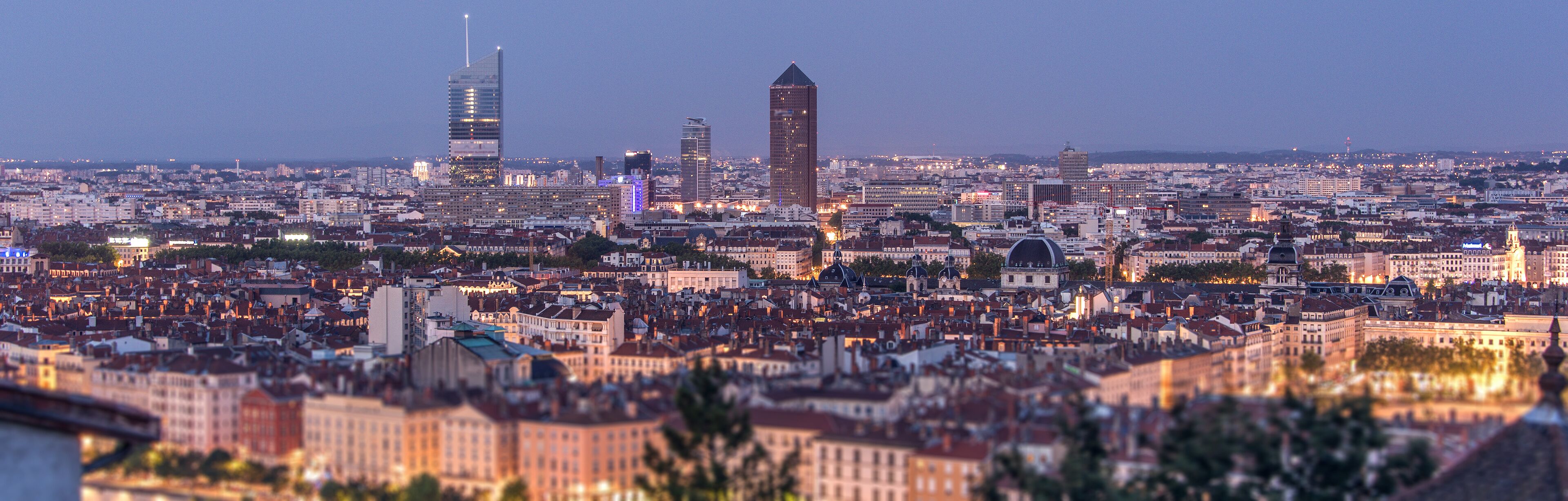 A cityscape at dusk with prominent modern skyscrapers and historic buildings.