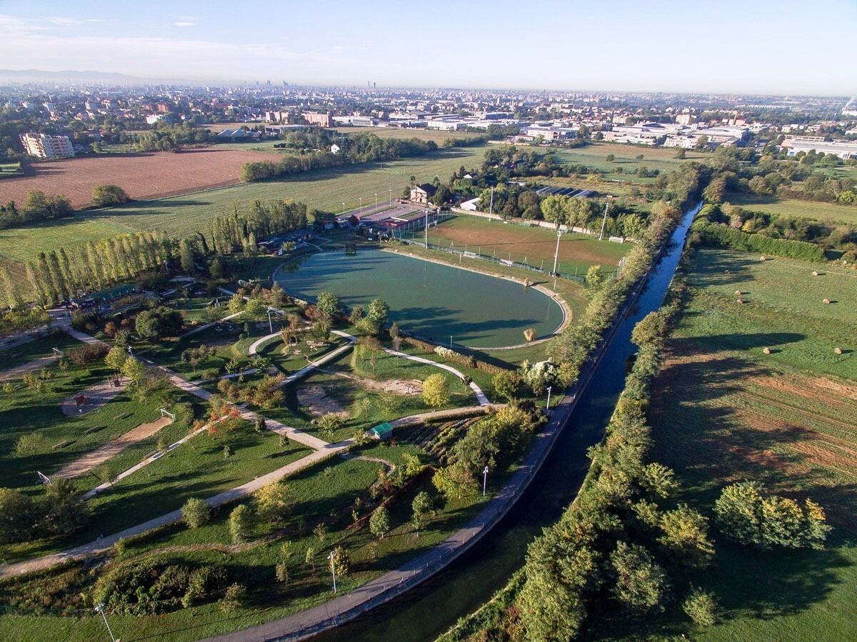Vista aérea de um parque com um caminho sinuoso, um rio e campos ao redor.