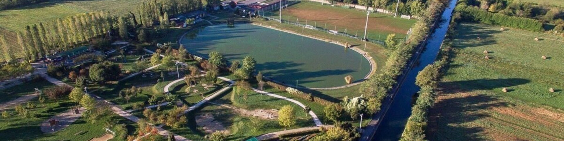 Vista aérea de um parque com um caminho sinuoso, um rio e campos ao redor.