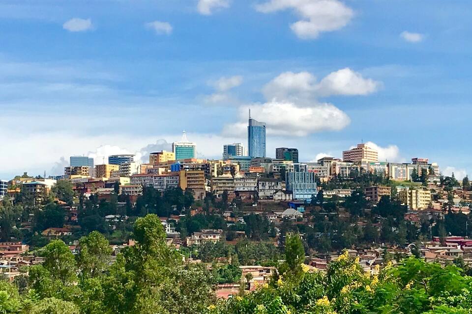 Un paysage urbain avec un gratte-ciel imposant, des bâtiments urbains denses et une végétation luxuriante environnante.