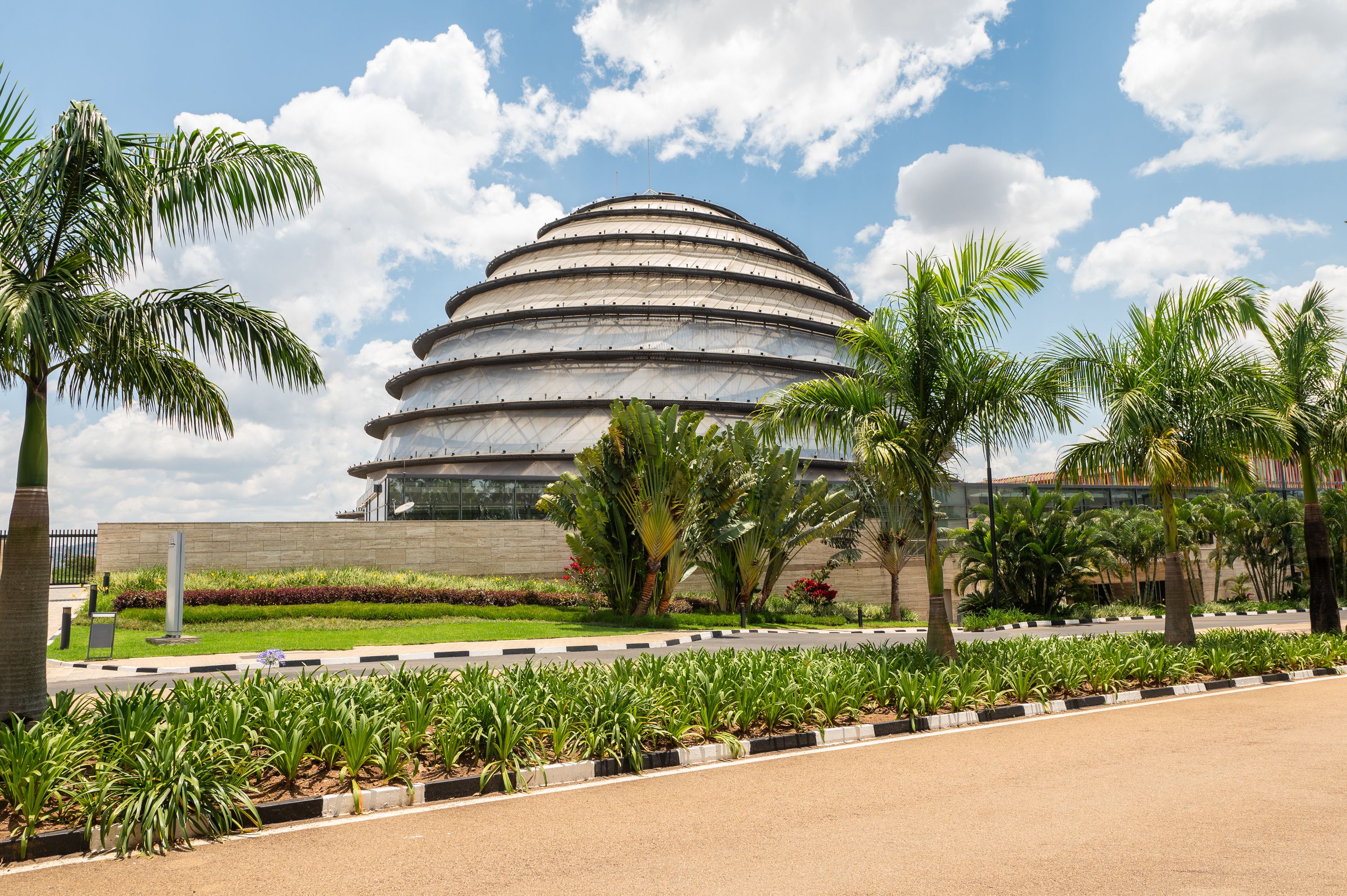 Un moderno edificio de diseño arquitectónico circular, rodeado por un jardín bien cuidado con palmeras y otra vegetación.