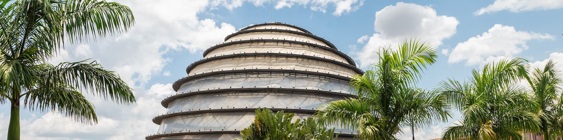 A modern architectural building with a circular design, surrounded by a well-maintained garden with palm trees and other greenery.