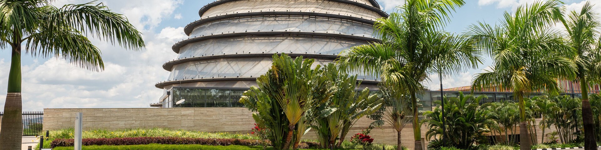 Un moderno edificio de diseño arquitectónico circular, rodeado por un jardín bien cuidado con palmeras y otra vegetación.