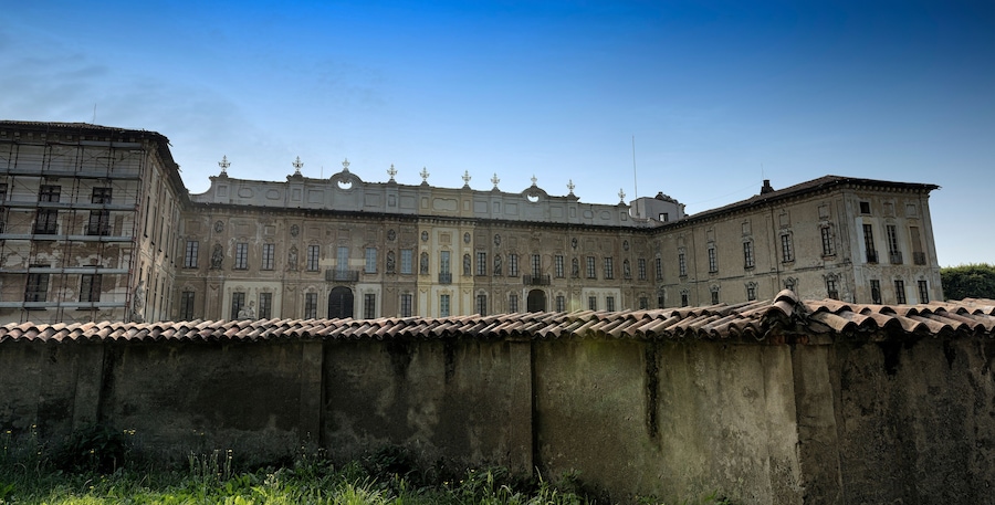 Un edificio histórico con arquitectura clásica, un gran muro al frente y un cielo azul despejado.