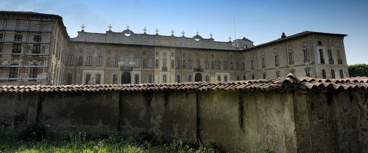 A historic building with classical architecture, a large wall in the foreground, and a clear blue sky.