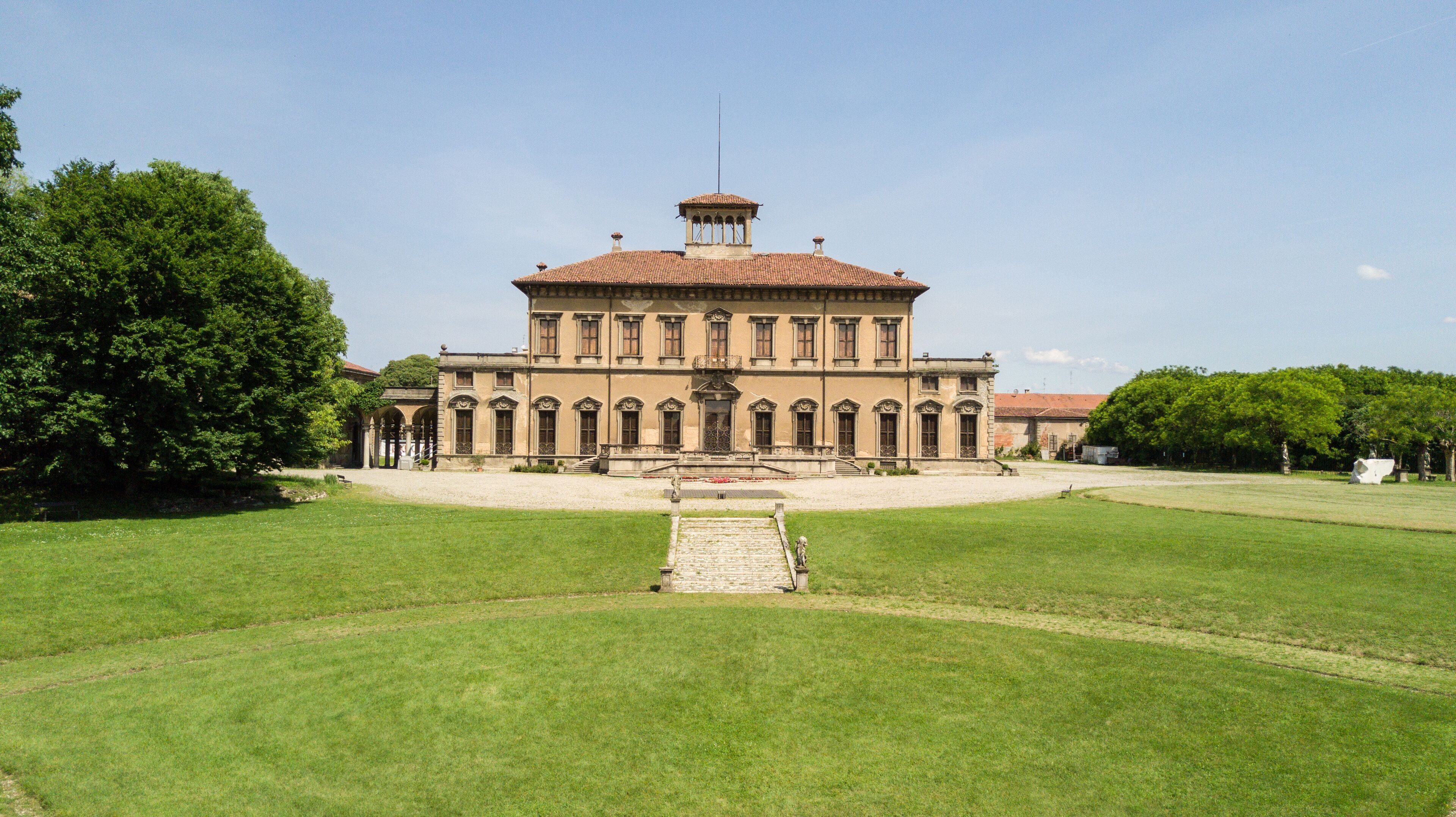 A large, historic building with a central staircase, surrounded by well-maintained lawns and trees.